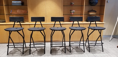 5 Black Folding Bar Chairs set up for panelists with shelving in background showing collectables